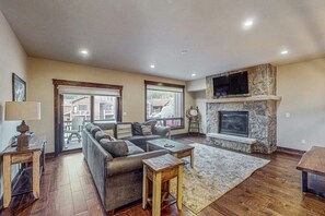 A living room with a stone fireplace, a sofa, a coffee table, and a view through large windows. - Beautiful townhome w/ balcony, hot tub & mountain views. Close to slopes (Keystone)