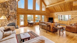 Un intérieur spacieux de chalet en bois, avec une cheminée en pierre, des meubles en bois et de grandes fenêtres.