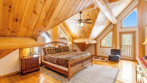 Une chambre avec un plafond en bois, un lit, une chaise et une fenêtre.