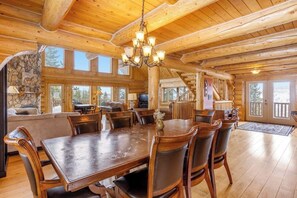 A spacious log cabin interior with a large dining table, wooden chairs, a chandelier, stone fireplace, and a staircase leading to a balcony. - Rare mountain-view log home with hot tub, fireplace & WiFi - near Breckenridge (Alma)