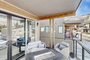 Ein Balkon mit Glastür, Korbmöbeln und einem Feuerkorb.