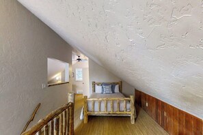 Ein Schlafzimmer mit schrägem Dach, einem Holzbettgestell und einem kleinen Fenster.