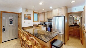 A kitchen with a granite countertop, stainless steel appliances, wooden cabinets, and a bar area with chairs. - Cozy condo w/ shared pool, hot tub & full kitchen - walk to lifts (Snowmass Village)