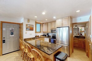 Eine Küche mit Granit Arbeitsplatte, Edelstahlgeräten, Holzschränken und einer Bar mit Sitzgelegenheiten.