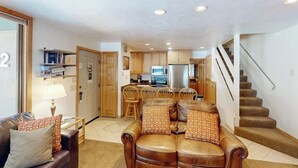 A modern living room with a leather sofa, a dining area, and a kitchen in the background. - Cozy condo w/ shared pool, hot tub & full kitchen - walk to lifts (Snowmass Village)
