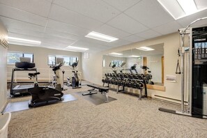 Une salle de sport équipée de matériel d’exercice, dotée d’un mur avec des miroirs et d’une fenêtre.