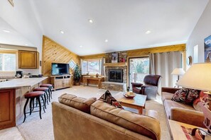 A spacious living area with a fireplace, a television, and a bar area with stools. - Remodeled ski-in condo with fireplace, hot tubs & gym (Breckenridge)