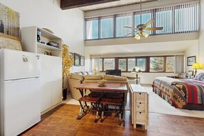 A spacious room with a dining table, a sofa, a bed, and a large window with blinds. - Studio condo w/ wifi, kitchenette, shared pool & hot tub - near golf & skiing (Durango)