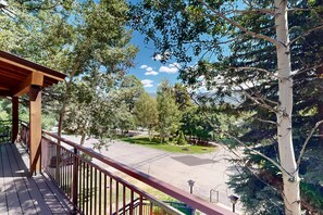 A wooden deck with a metal railing overlooking a parking area and a green landscape with trees. - Studio condo w/ wifi, kitchenette, shared pool & hot tub - near golf & skiing (Durango)