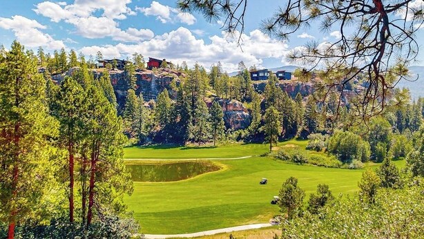 Ein Golfplatz mit Teich, umgeben von Bäumen und Gebäuden auf einer Anhöhe.