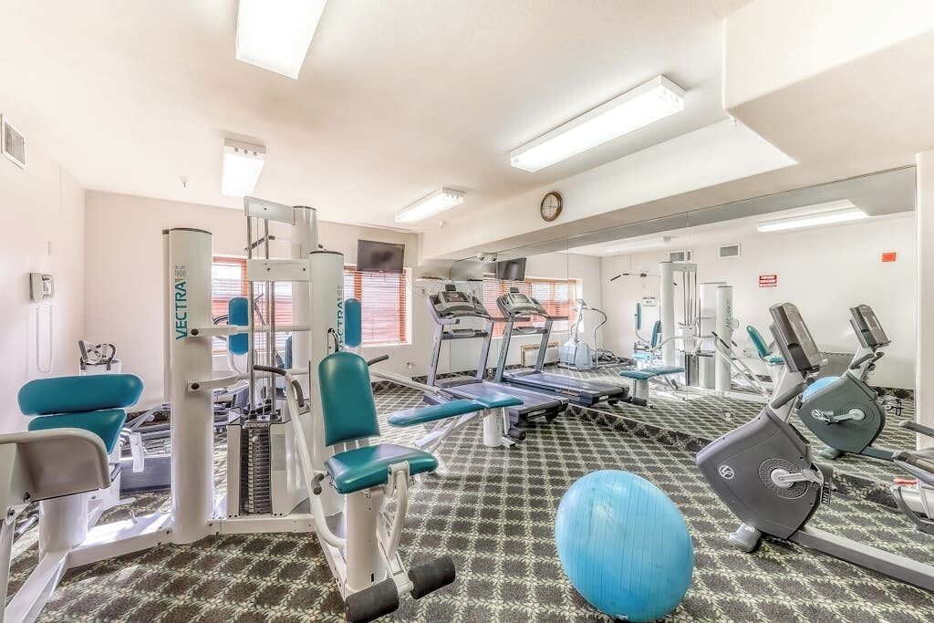 A gym with exercise equipment, a mirrored wall, and a patterned floor.