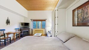 A bedroom with a large bed, a television, a fireplace, and a window with a view of trees. - Cozy resort studio - Walk to lifts, shops, restaurants & entertainment (Keystone)