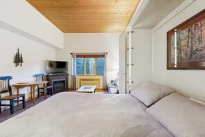 A bedroom with a large bed, a television, a fireplace, and a window with a view of trees. - Cozy resort studio - Walk to lifts, shops, restaurants & entertainment (Keystone)