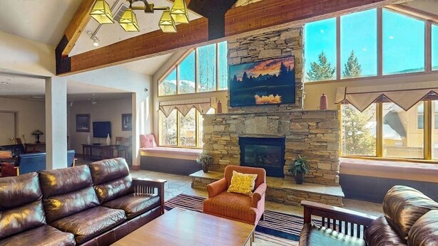 A spacious living room with leather sofas, a wooden coffee table, and a stone fireplace. - Cozy resort studio - Walk to lifts, shops, restaurants & entertainment (Keystone)