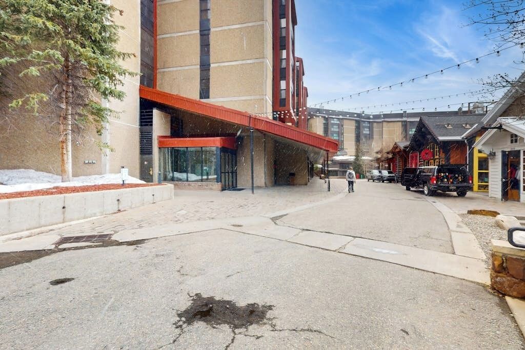 Un edificio dal design architettonico moderno, con ingresso coperto e una strada con veicoli parcheggiati.