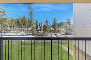 Ein Balkon mit Blick auf eine Rasenfläche, Bäume und ein entferntes Gebäude.