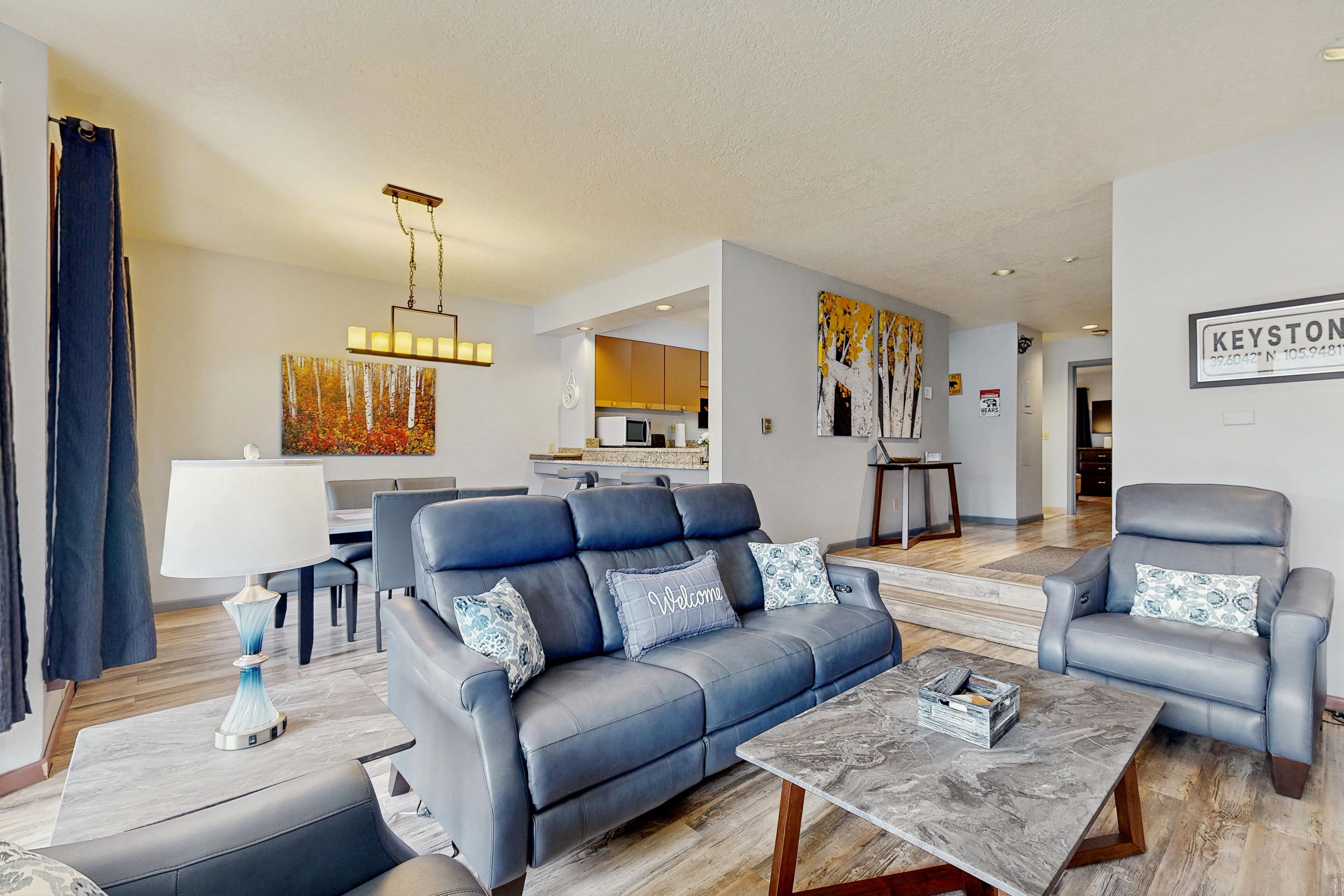 A modern living room with a blue sofa, a coffee table, and a dining area in the background.