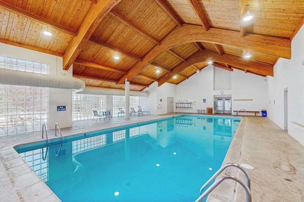 An indoor swimming pool with a wooden ceiling, clear glass windows, and a 'NO GLASS' sign.