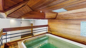 Interior de madeira com piscina, corrimão e placa de alerta.