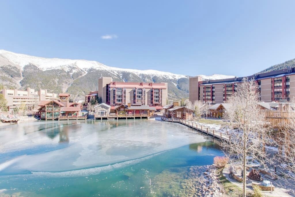 Een hotel met uitzicht op een meer, met besneeuwde bergen op de achtergrond en een houten steiger die in het water reikt.