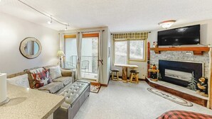 A living room with a fireplace, a television, a sofa, and a dining area. - Ski-In/Ski-Out Studio with Gas Fireplace & Shared Pool, Hot Tub, Gym,  Game Room (Winter Park)