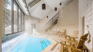 An indoor swimming pool with clear glass walls, wooden Adirondack chairs, and a staircase leading to an upper level. - Ski-In/Ski-Out Studio with Gas Fireplace & Shared Pool, Hot Tub, Gym,  Game Room (Winter Park)