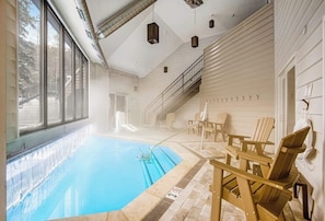 Ein Hallenbad mit großen Glaswänden, Holz-Adirondack-Stühlen und einer Treppe, die zu einer oberen Ebene führt.