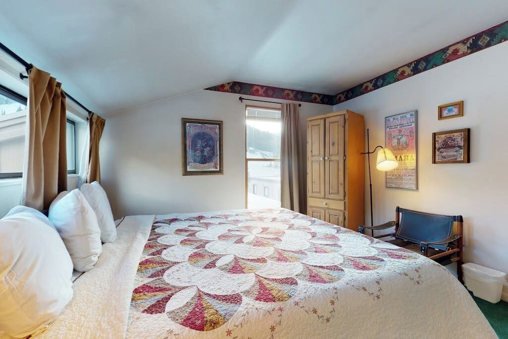 A hotel room with a bed, a desk, a chair, a lamp, and a window with curtains.