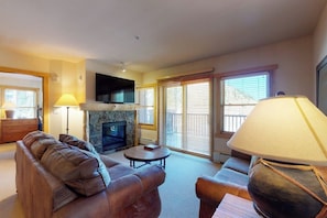 A living room with a fireplace, sofa, armchair, and lamp. - Chalet next to gondola w/shared fitness center, hot tub, & sauna (Copper Mountain)