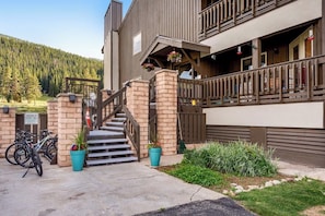 A two-story building with a staircase leading to the entrance, a balcony with railings, and a parking area with bicycles. - Mountain view condo w/gas fireplace, shared outdoor pool, and free WiFi (Copper Mountain)
