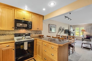A kitchen with wooden cabinets, a microwave, stove, and a dining area with chairs and a table. - Mountain view condo w/gas fireplace, shared outdoor pool, and free WiFi (Copper Mountain)