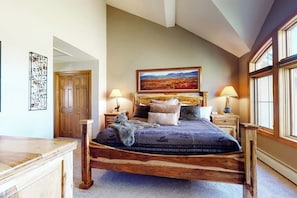 A bedroom with a wooden bed, a painting above the bed, and a window on the right. - Ski-in ski-out townhouse w/mountain views, gas fireplace, WiFi (Copper Mountain)