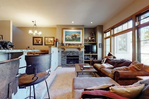 A living room with a fireplace, a sofa, a coffee table, and a dining area with chairs. - Ski-in ski-out townhouse w/mountain views, gas fireplace, WiFi (Copper Mountain)