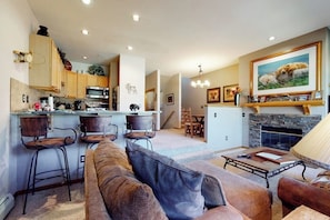 A modern kitchen with bar stools, a dining area with a fireplace, and a living room with a sofa and coffee table. - Ski-in ski-out townhouse w/mountain views, gas fireplace, WiFi (Copper Mountain)