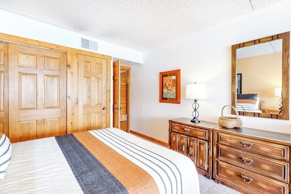 Un dormitorio con cama, armario de madera, cómoda, espejo y un cuadro en la pared.