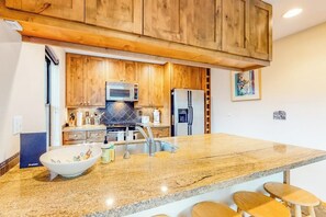 A kitchen with wooden cabinets, a granite countertop, a microwave, a refrigerator, and a sink.