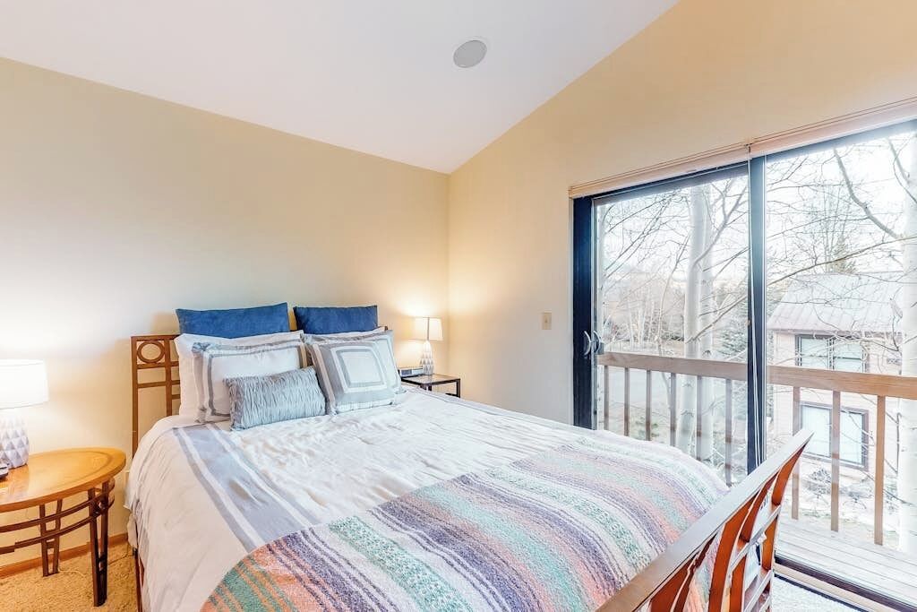 Quarto com cama, mesa de cabeceira, cadeira, janela com vista e varanda.