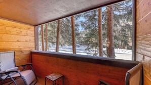 A wooden cabin with a bench, a small table, and a window overlooking a snowy forest. - Cozy, comfortable condo with pool & hot tubs - walk to lifts & Main Street (Breckenridge)