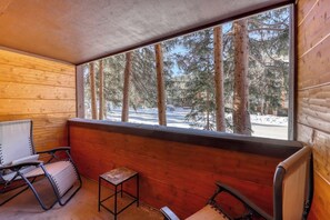 Eine Holzhütte mit einer Bank, einem kleinen Tisch und einem Fenster mit Blick auf einen verschneiten Wald.