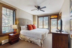 Ein Hotelzimmer mit einem großen Bett, einem Deckenventilator, einem Fernseher und einem Fenster mit Jalousien.