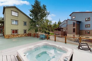 Ein Whirlpool auf einer Holzterrasse mit Steinunterbau, umgeben von einem Holzzaun und angrenzend an ein Gebäude mit Steinbasis.