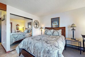 Quarto com uma cama grande, um espelho, relógio fixado na parede, quadro emoldurado e mesa de cabeceira com abajur.