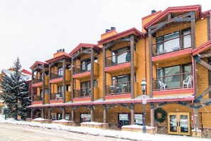Um hotel com vários andares, varandas, janelas amplas e o chão coberto de neve.