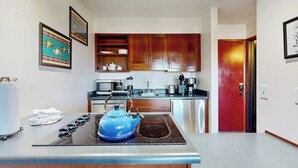 A modern kitchen with wooden cabinets, a microwave, a kettle, and a red door. - Riverfront studio with mtn view, balcony, & fireplace (Breckenridge)