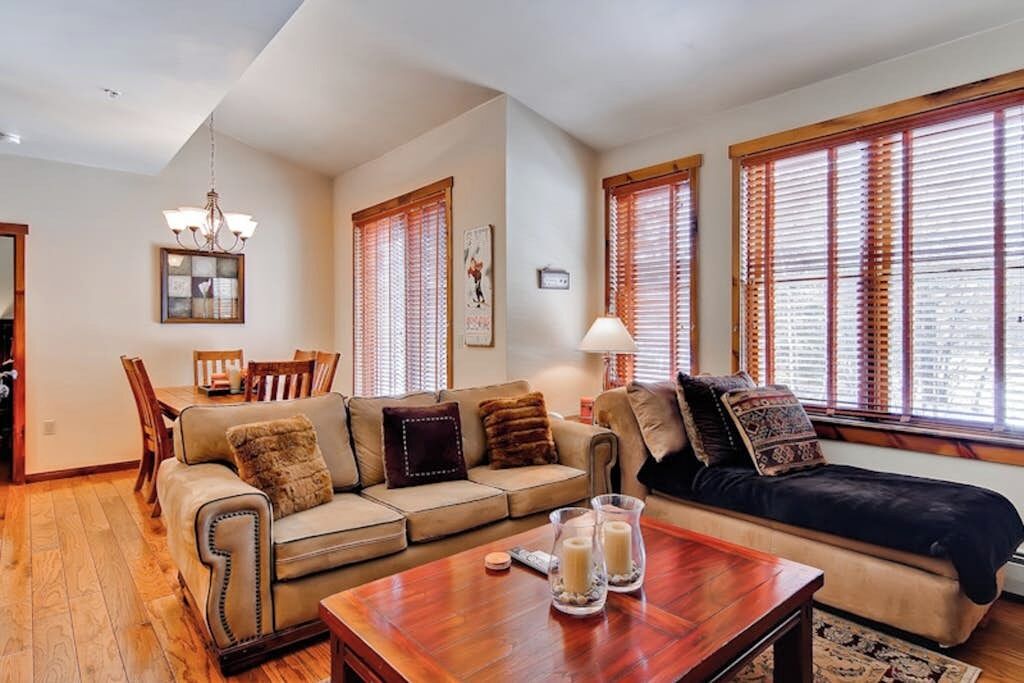 A living room with a sofa, a coffee table, and a dining area with chairs and a chandelier.
