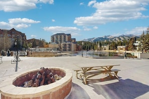 A courtyard with a fire pit, picnic table, and a view of mountains. - Modern condo, shared hot tub, steps to QuickSilver Super Chair lift (Breckenridge)