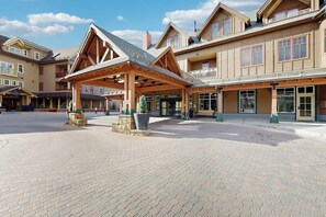 A building with a covered entrance, stone planters, and a paved plaza. - Modern condo, shared hot tub, steps to QuickSilver Super Chair lift (Breckenridge)