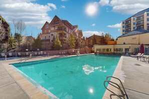 A swimming pool with a clear blue water, surrounded by buildings and trees. - Modern condo, shared hot tub, steps to QuickSilver Super Chair lift (Breckenridge)