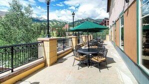 Une terrasse extérieure avec des tables et des chaises, un parasol vert et une vue sur les montagnes.