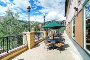 Un patio exterior con mesas y sillas, una sombrilla verde y vistas a las montañas.